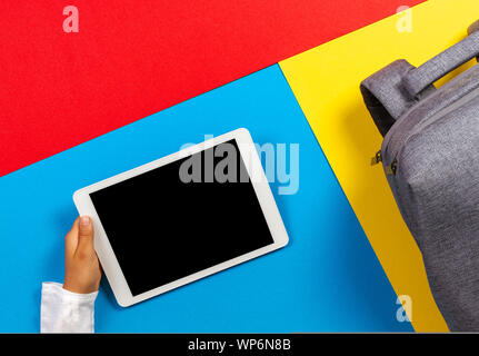 Top view to kid hands with tablet computer and gray backpack on colorful background Stock Photo