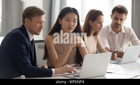 Mixed race groups of employees sitting at shared table, working on different projects. Stock Photo