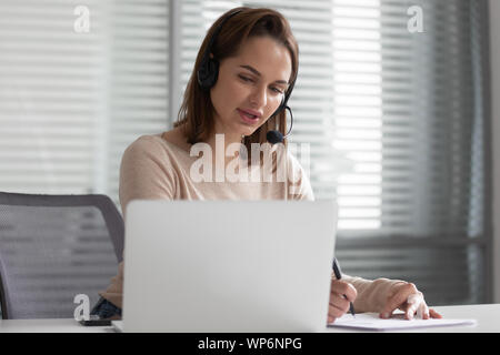 Serious young female executive manager wearing earphones, holding video call. Stock Photo
