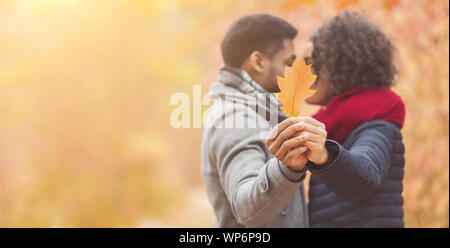 Romantic couple hiding behind oak leaf kissing in autumn park Stock Photo