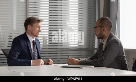 Two multiracial focused male partners discussing company development strategy. Stock Photo