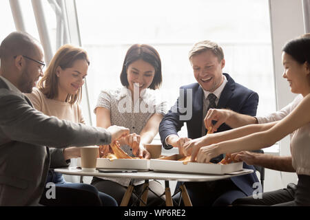 Happy mixed race company workers sharing lunch, eating pizza. Stock Photo