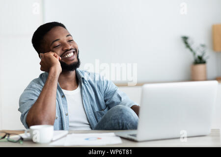 African guy talking on phone, working on laptop in office Stock Photo