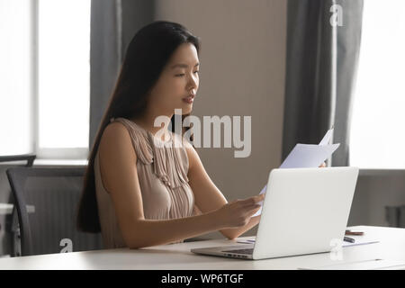 Serious focused busy young female asian employee reading financial report. Stock Photo