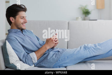 Happy Man Using Smartphone Browsing Internet Lying On Couch Stock Photo