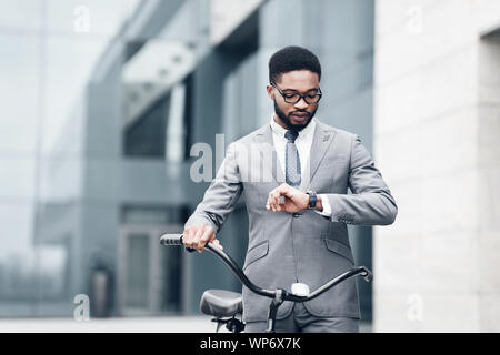 Afro businessman checking time, riding to office on bike Stock Photo