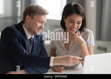 Smiling middle aged team leader helping korean female happy intern. Stock Photo