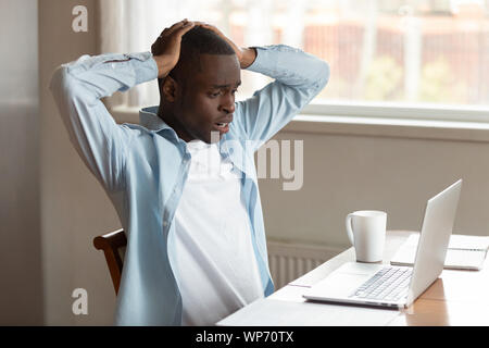 Frustrated biracial man shocked by virus attack on laptop Stock Photo