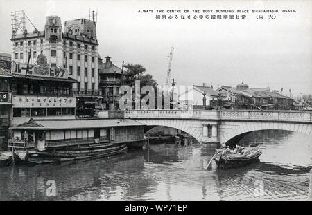 [ 1910s Japan - Shinsaibashi Bridge in Osaka ] —   Shinsaibashi Bridge across the Nagahori canal in Osaka, Japan.  The stone bridge in this image was opened in 1909 (Meiji 42) and replaced a German made steel bridge in use since 1873 (Meiji 6).  The white building is the Ishihara Tokeiten (石原時計店). This well-known retailer of watches moved here in 1915 (Taisho 4). Besides watches, the shop sold jewelry, and imported luxury items like cameras and musical instruments.  20th century vintage postcard. Stock Photo