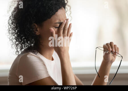 Exhausted biracial woman take off glasses suffering from migraine Stock Photo