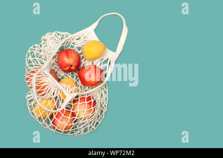 Juicy ripe peaches and apricots in eco bag on a blue background. Copy space. Zero waste concept, plastic-free, eco-friendly shopping, vegan Stock Photo