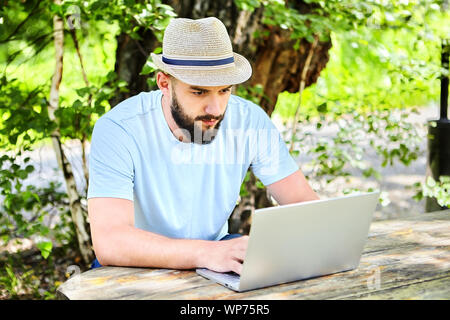 A rural businessman, agronomist scientist is studying a farming program on a laptop. A farmer sits at a table outdoors and looks at a notebook screen. Stock Photo