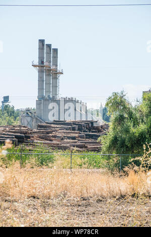 A large lumber mill in Southern Oregon with three large smoke stacks and plles of tree trunks ready for processing in the foreground.
