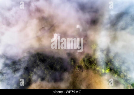 THick white fog covering remote agricultural farm in Kangaroo Valley of Australia. Aerial  top down view over gum-trees and paddocks around farm house Stock Photo