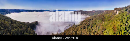 Thick white fog creeping in the Kangaroo valley between tall sandstone cliffs of surrounding mountains - elevated aerial panoramic view above the clou Stock Photo