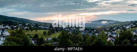 Wide panoramic view over the mountainous village of Grafschaft in the winter sports region of Sauerland, Germany, during colourful sunset Stock Photo