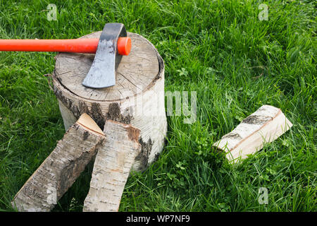 Stump with an splitting axe and firewood on the grass. Birch logs