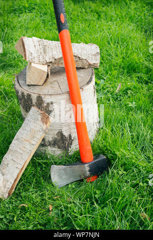 Splitting axe at a stub and firewood on the grass. Birch logs