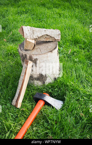 Splitting axe lying on the grass and nearby birch firewood. Preparation for winter