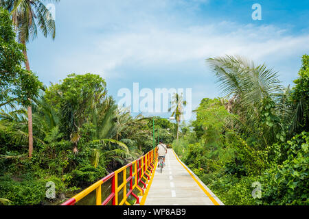 Cycling in Bang Krachao, known as the Green Lung of Bangkok. A young man cycles along the pathway surrounded by lush tropical vegetation. Stock Photo