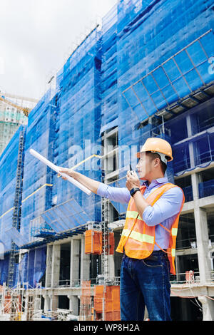 Contractor pointing with scroll in his hand and talking on walkie-talkie Stock Photo