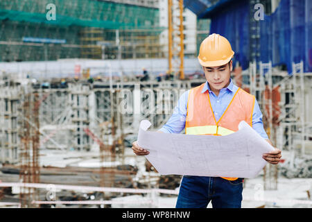Serious professional Asian civil engineer examining building plan at working area Stock Photo