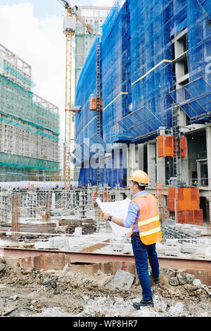 Civil engineer checking building blueprint when working on new project at construction site Stock Photo