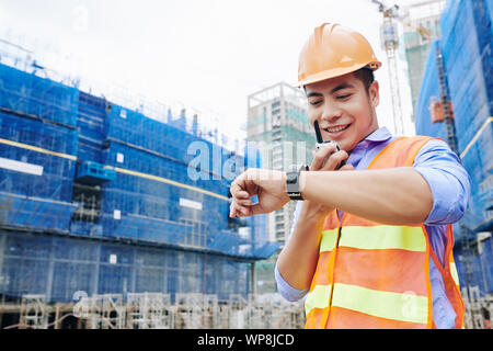 Smiling Vietnamese contractor talking to workers via walkie-talkie and making sure that everything will be done right on time Stock Photo