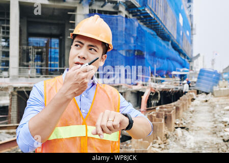 Portrait of frowning serious contractor talking on walkie-talkie when standing at construction site of new building Stock Photo