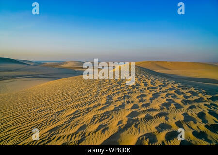 Desert at sunrise rolling wind rippled sand dunes under blue sky. Stock Photo