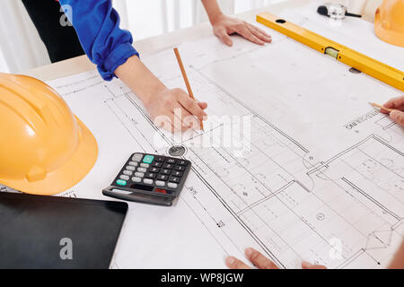 Hands of contractor in blue overall leaning on table and examining building blueprint to plan work for upcoming week Stock Photo
