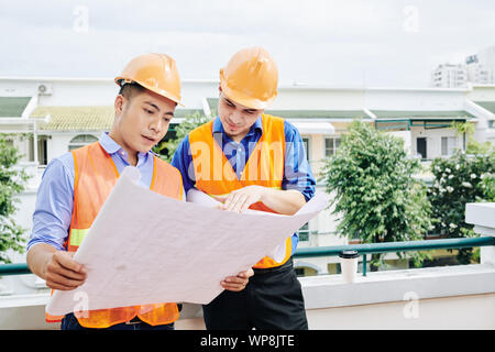 Vietnamese engineer discussing building blueprint with contractor when they are working on project at construction site Stock Photo
