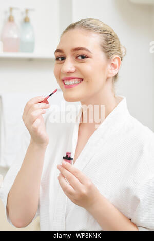 Portrait of happy young woman applying matte mauve liquid lipstick when doing make-up Stock Photo