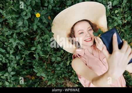 Happy pretty young woman lying on grass and talking selfies on smartphone, view from above Stock Photo