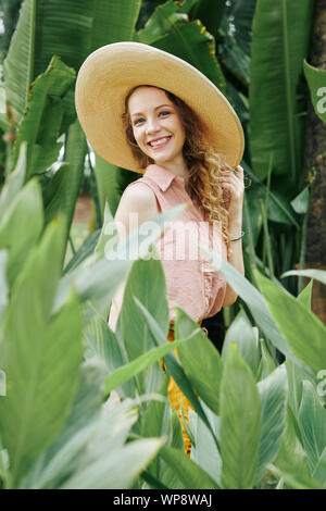 Beautiful young woman in big straw hat enjoying walking among flowers in summer garden Stock Photo