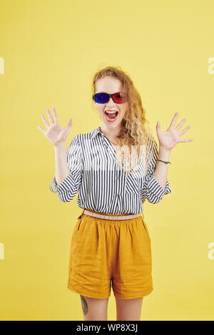 Happy young woman in paper 3D glasses shouting from excitiment, isolated on yellow background Stock Photo