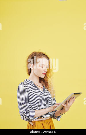 Serious young female entrepreneur using application on tablet computer for communication with coworkers and business partners Stock Photo