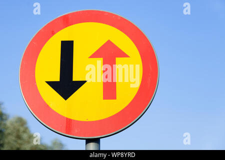 traffic sign with red and black arrow on yellow background. Here you have to wait for oncoming traffic. Stock Photo