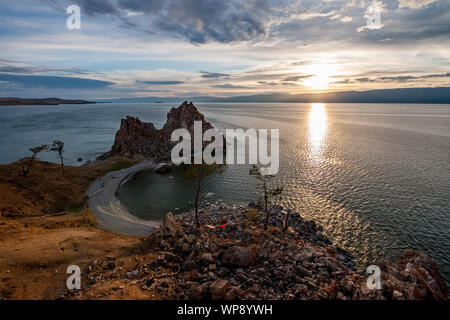 Sunset on Lake Baikal overlooking the high cliff of Shamanka and beautiful sky. There are stones and several trees on the shore. Stock Photo