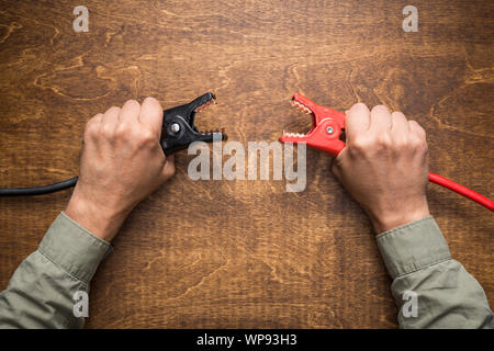 Hands holding car battery charging clamps. Concept of opposite polarity conflict or interaction. Stock Photo