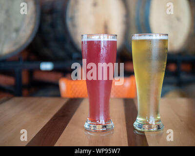 Pink and blond tall cold glasses of beer on table in front of barrels in brewery Stock Photo