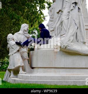 Young man sitting on a monument to Ludovic Trarieux, commemorating  the foundation of the Human Rights League, Square Claude-Nicolas-Ledoux Paris, FR. Stock Photo