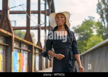 Laughing vivacious young African woman wearing braided hair extensions and a stylish wide brimmed straw hat Stock Photo