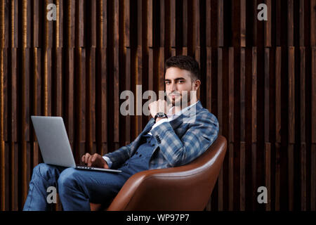 Young successful businessman is working behind a laptop while sitting in a loft office. bearded man working on a laptop. Stock Photo