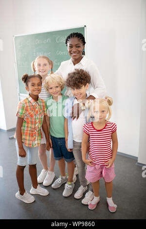 Loving smiling teacher hugging her cute smart pupils Stock Photo