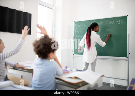 Dark-skinned teacher writing down on blackboard for children Stock Photo