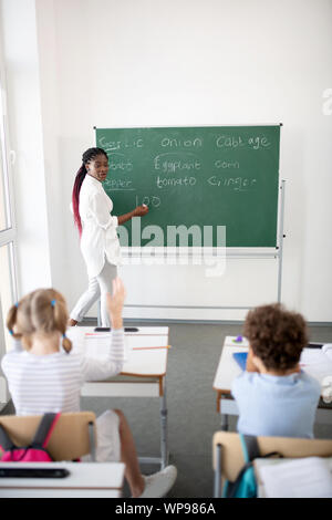 Teacher standing near blackboard and explaining new material Stock Photo