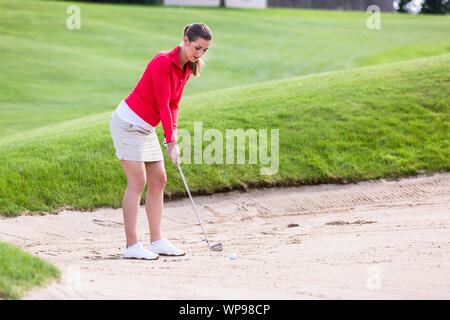 Female golfer hitting golf ball on bunker Stock Photo