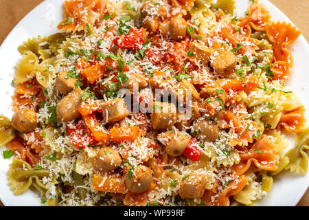 Farfalle pasta with sausages, vegetables and grated parmesan on plate - top view