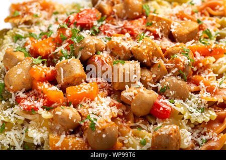 Farfalle pasta with sausages, vegetables and grated parmesan on plate - close up view